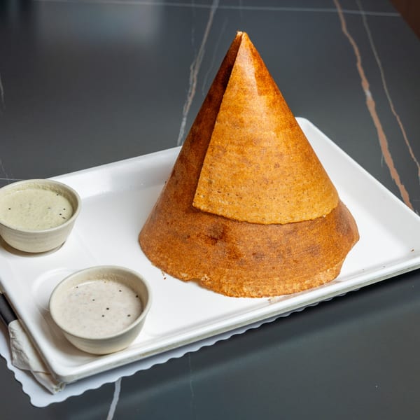 Crispy golden-brown cone dosa with two small bowls of chutney on a white rectangular plate.