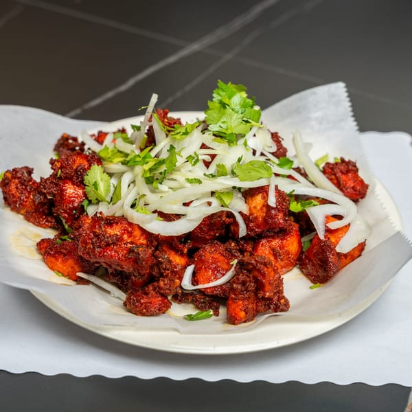 Maa Kitchen's Chicken 65, a vibrant red Indian dish, garnished with fresh cilantro and sliced onions.
