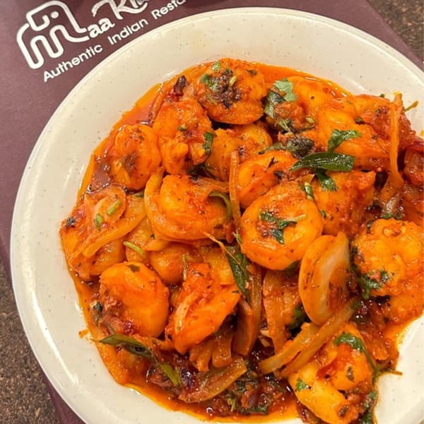 A close-up of Maa Kitchen's Indian shrimp dish with onions and cilantro in a rich red sauce.