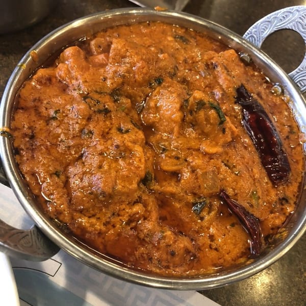 A close-up of a vibrant orange Indian curry, possibly butter chicken, in a metal serving bowl.