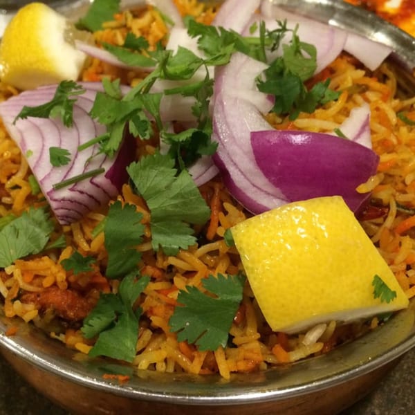 Close-up of Maa Kitchen's Indian biryani, garnished with red onions, cilantro, and lemon wedges.