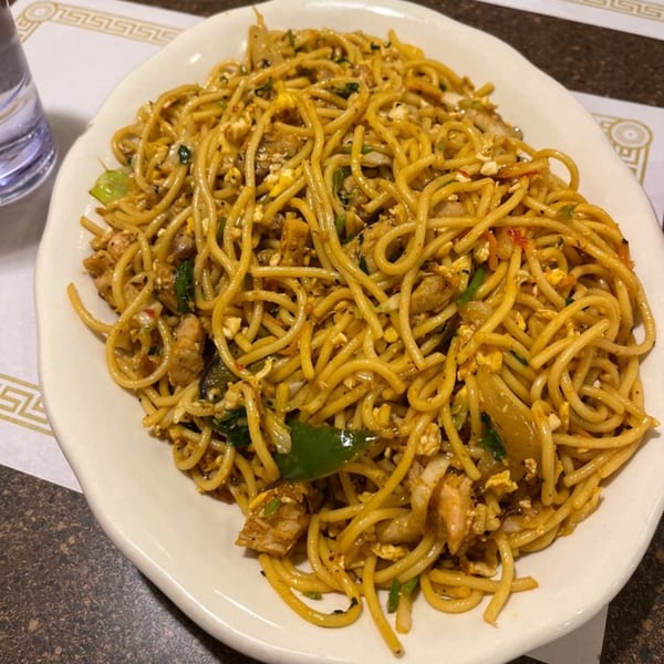 A large white plate of Maa Kitchen's Indian-style noodles with chicken, egg, and vegetables.