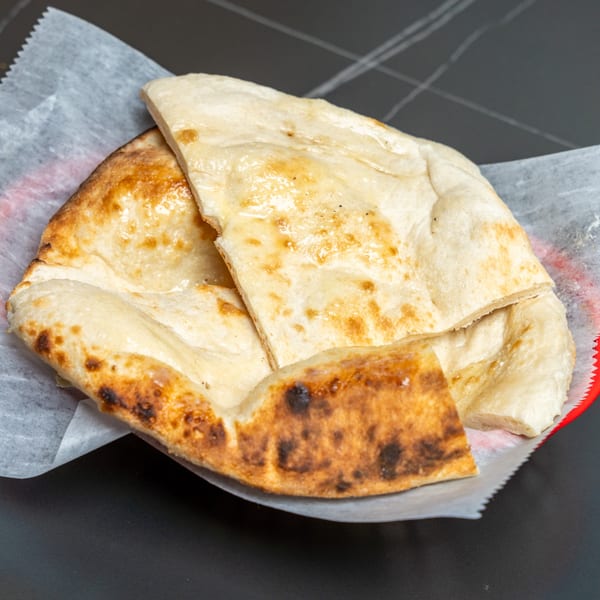 Golden brown Indian naan bread, some pieces cut, served in a red basket lined with white paper.